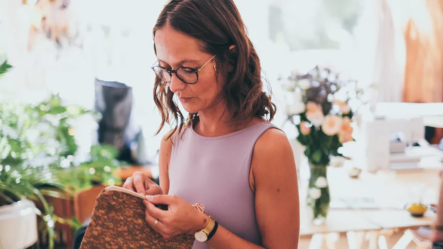 Woman sewing in a bright room with plants.