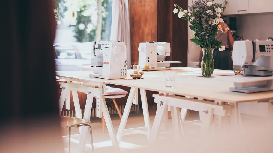 Sewing machines on wooden tables in bright room.