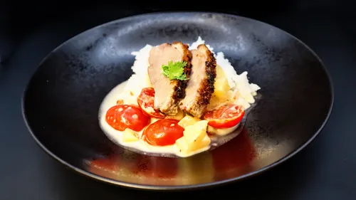 Sliced meat on vegetables, black plate.