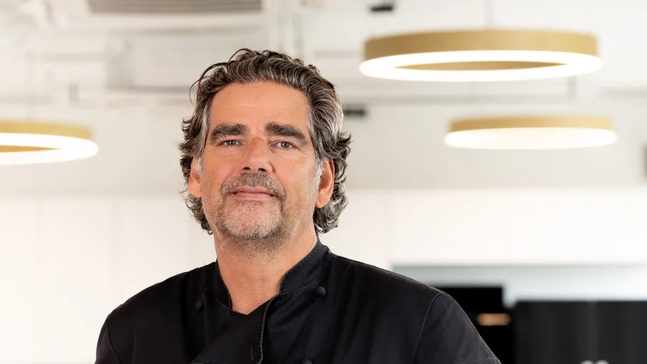 Man in chef coat stands in kitchen.