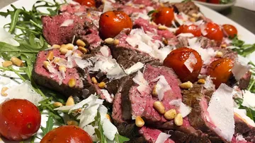 Sliced steak with arugula, cherry tomatoes, pine nuts.
