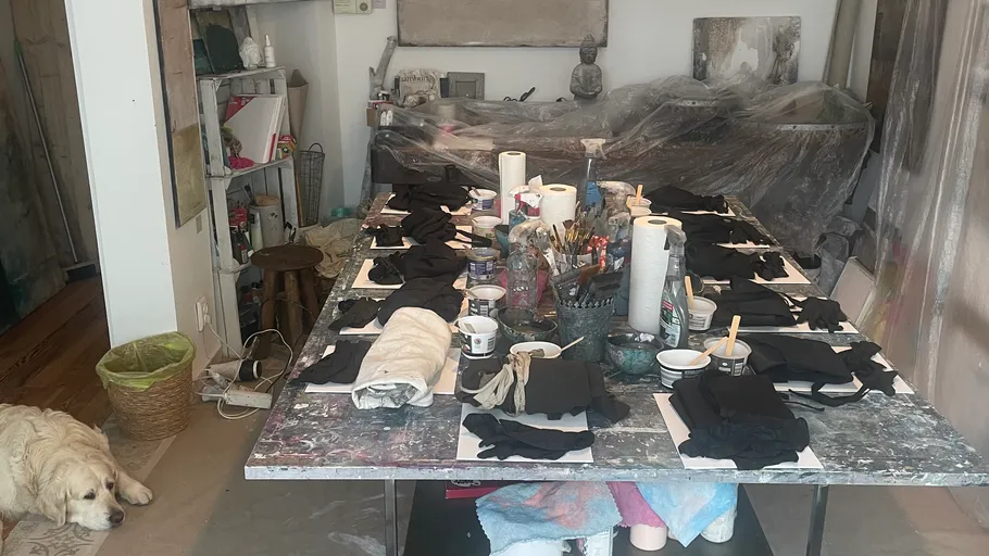 Kunstbedarf auf einem überfüllten Tisch, schlafender Hund in der Nähe.