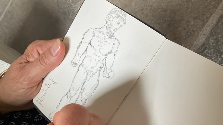 Hands holding sketchbook with ancient sculpture drawing.