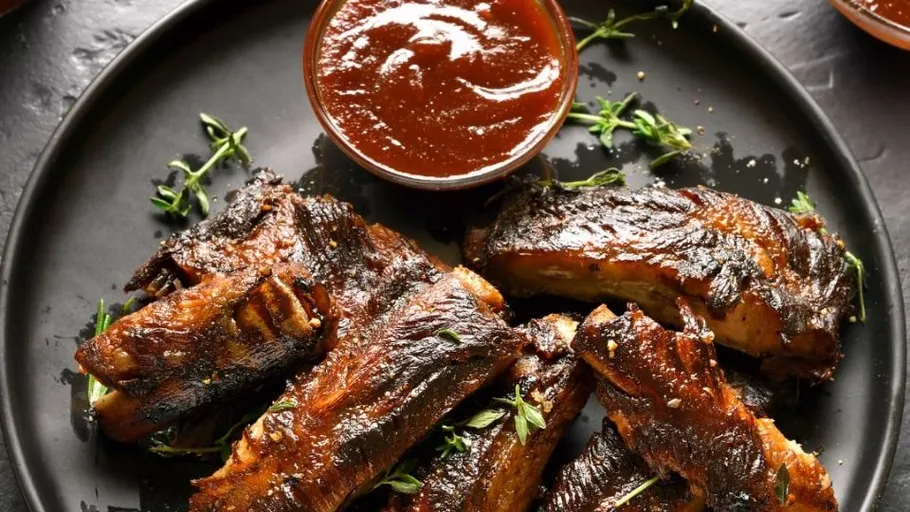 Grillrippchen mit Soße auf schwarzem Teller.