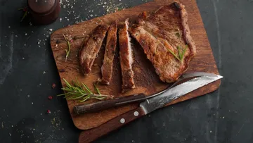 Sliced steak on wooden board with rosemary.