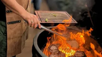Person grilling meat on flaming barbecue.