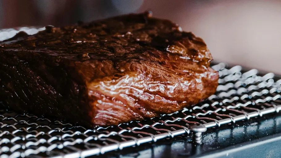 Grilled steak cooking on metal grate.