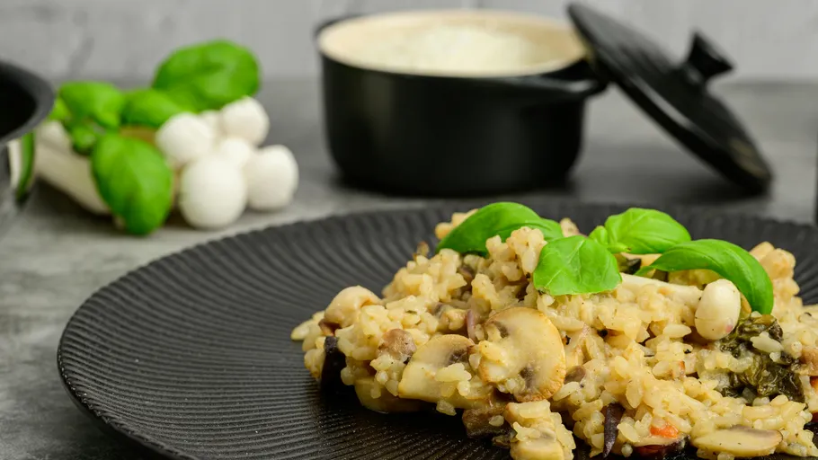 Pilzrisotto mit Basilikum auf schwarzem Teller.