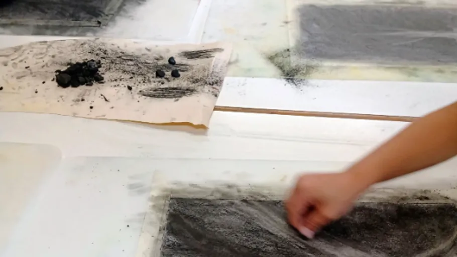 Hand smudging charcoal on white paper surface.