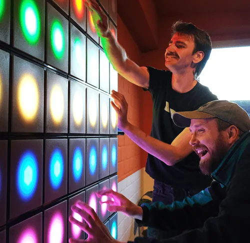 Two men interacting with colorful light wall.