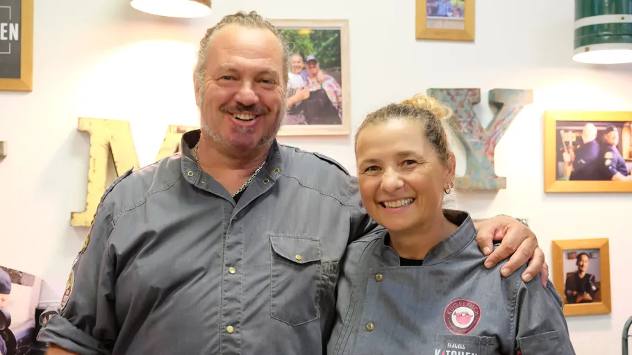 Two smiling chefs in front of framed photos.
