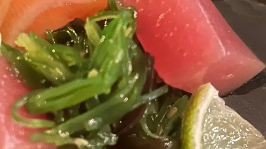 Sliced tuna with seaweed and lime on plate.