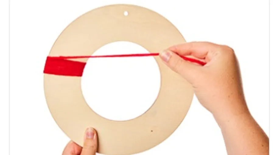 Hands wrapping red yarn around wooden ring.