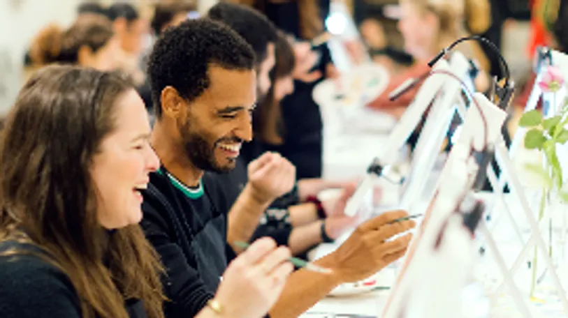 People laughing, interacting around computers, indoor setting.