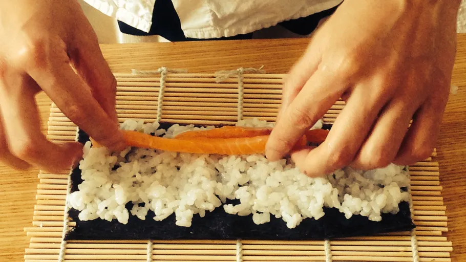 Hands rolling sushi on bamboo mat.