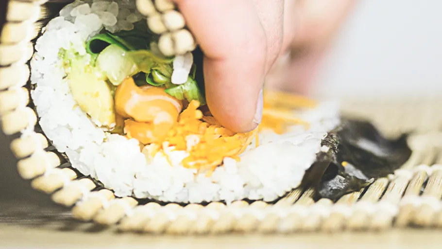 Hand rollt Sushi mit Bambusmatte.