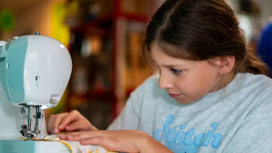 Girl sewing with a machine indoors.