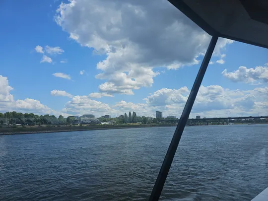 River view from boat, cloudy sky, distant buildings.