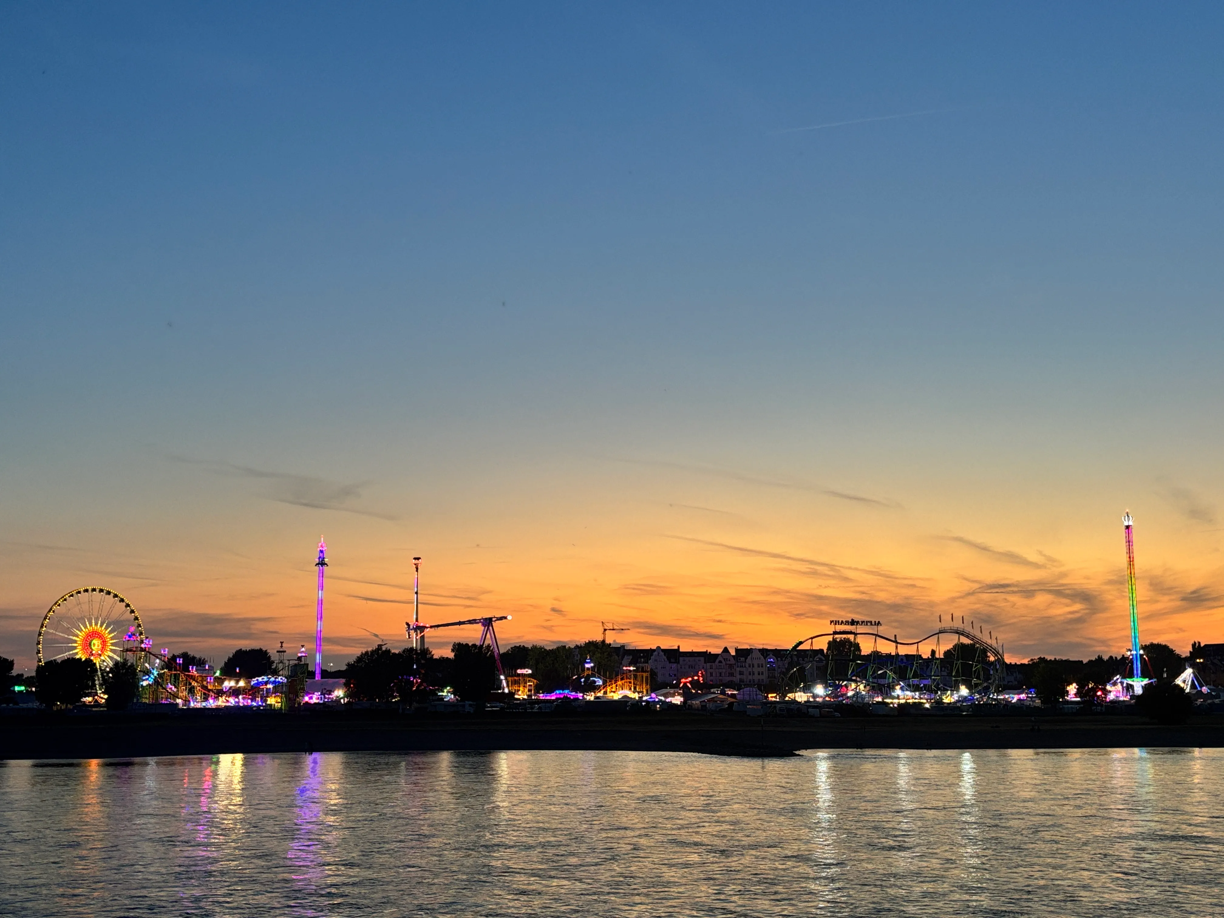 Vergnügungsparklichter bei Dämmerung am Wasser.