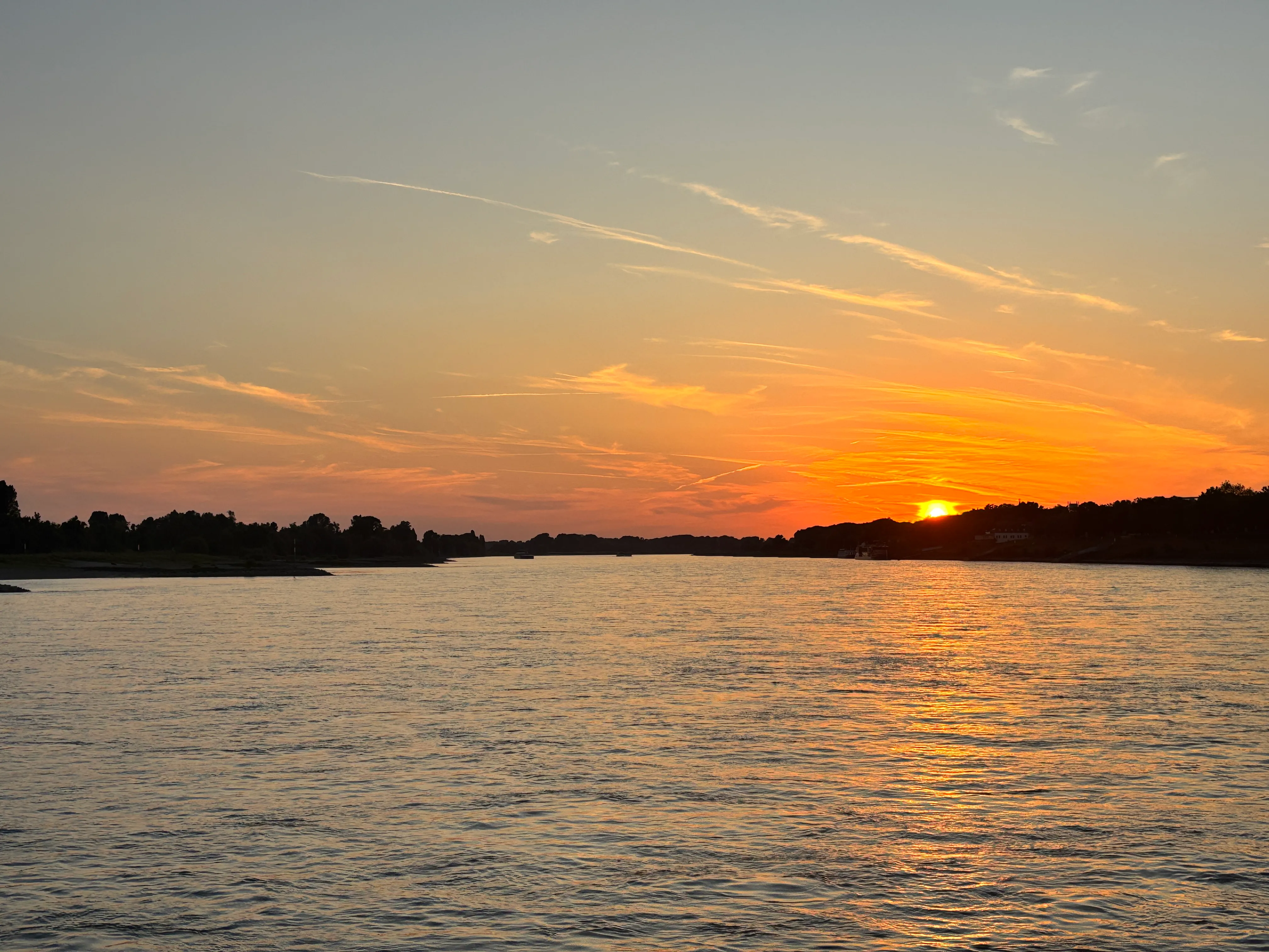 Sonnenuntergang über ruhigem Fluss und fernen Hügeln.