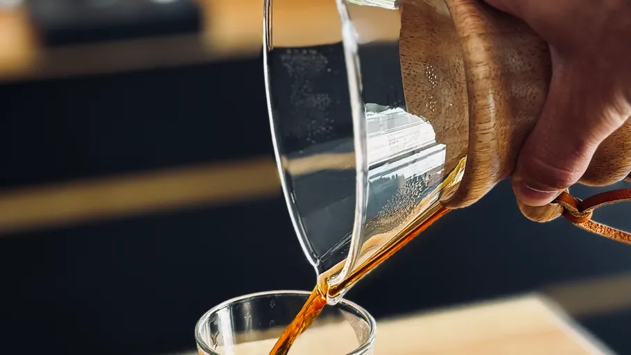 Hand gießt Kaffee aus Chemex in Glas.