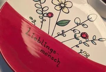 Dekorative Platte mit Blumen und "Lieblingsmensch"-Text.