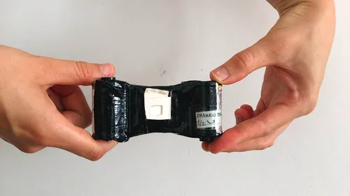 Hände halten schwarzes bandumwickeltes Objekt drinnen.