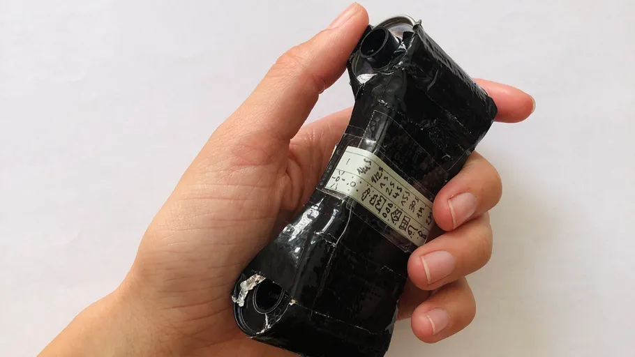 Hand hält schwarzen zylindrischen Gegenstand mit Klebeband.