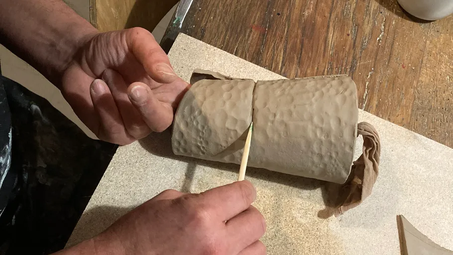 Hände formen Tonzylinder auf Holztisch.