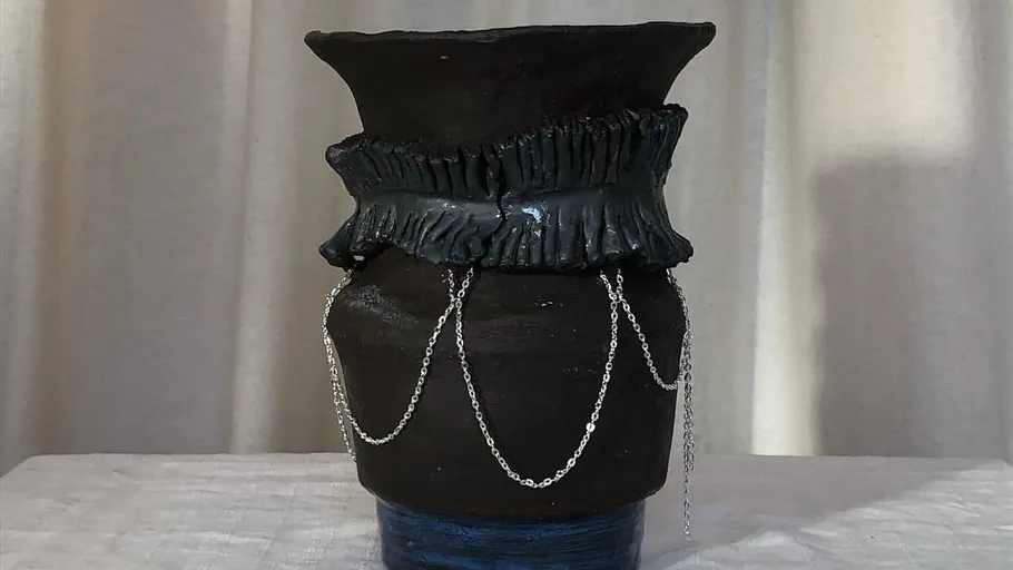 Schwarze Keramikvase mit Ketten auf Tisch.