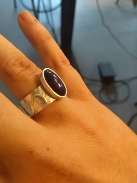 Hand with silver ring, blue stone, indoors.