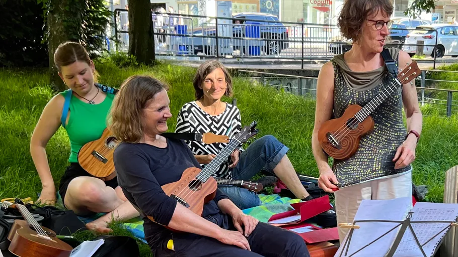 Frauen spielen Ukulelen auf dem Gras sitzend.