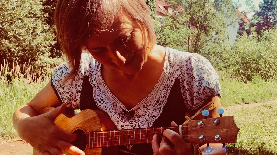Woman playing ukulele outside in sunny park.
