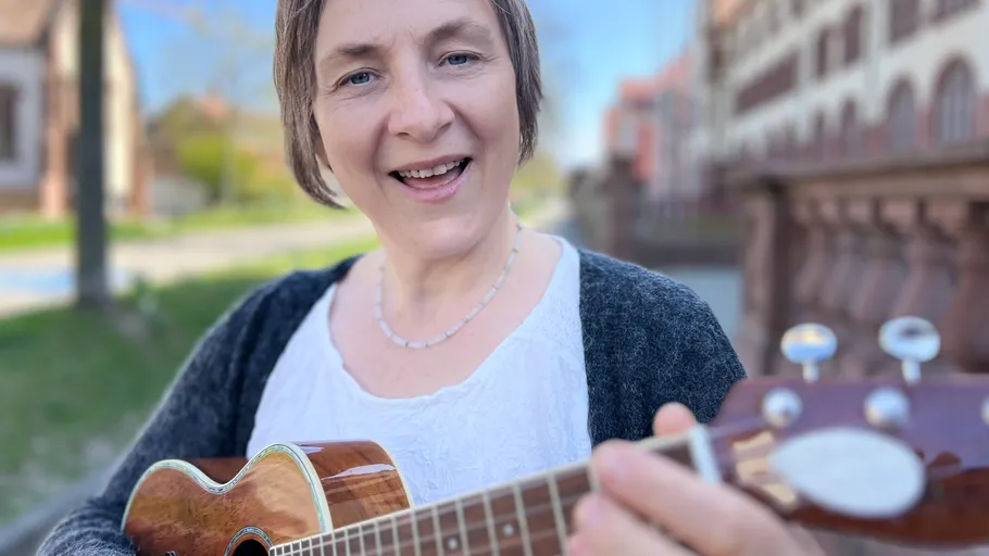 Woman smiling, playing ukulele outdoors, street background.