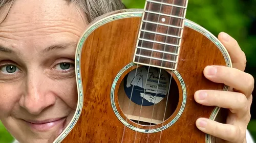 Person hält Ukulele nah am Gesicht im Freien.