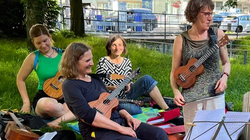 Four women playing ukuleles in a park.