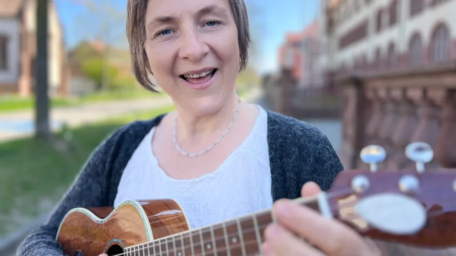 Person playing guitar outdoors smiling.