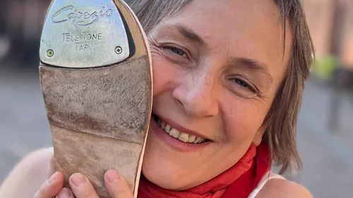 Woman smiles holding tap shoe to face.