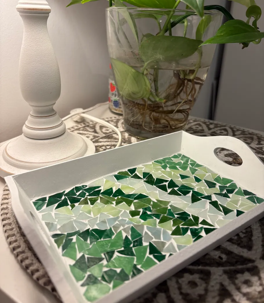 Mosaiktablett auf Tisch neben Lampe und Pflanze.