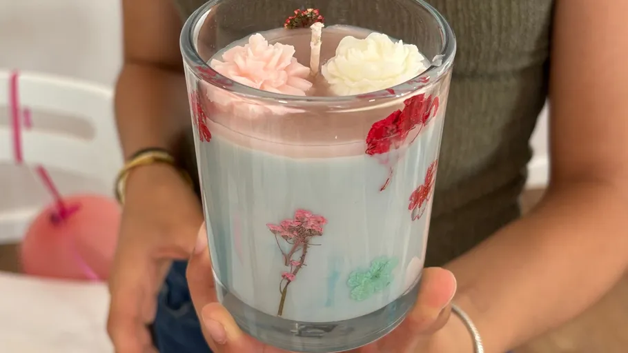 Hand hält Kerze mit Blumen in Glas.