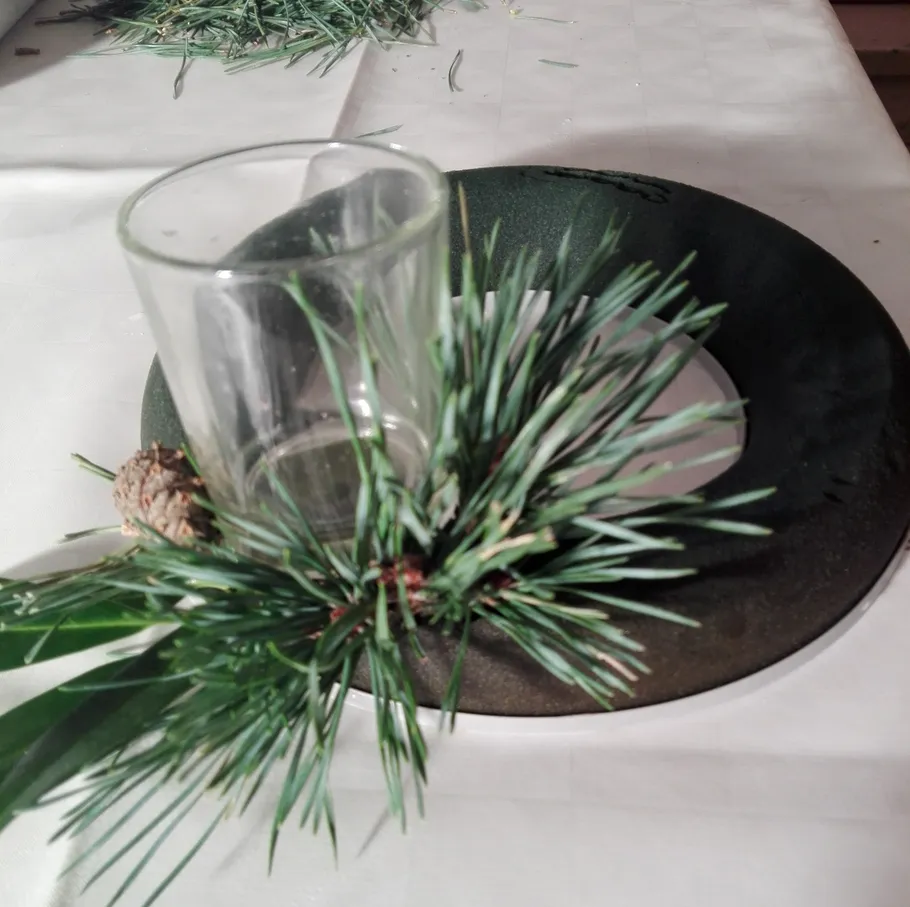 Glass with pine branches on table.