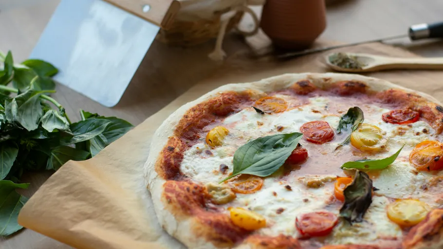Pizza mit Basilikum und Tomaten auf Tisch.