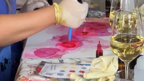 Person painting with ink, wine glasses nearby.