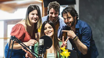 Vier Personen lächeln um ein Mikrofon im Studio.