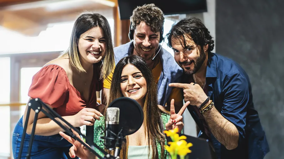 Vier Personen lächeln um ein Mikrofon im Studio.