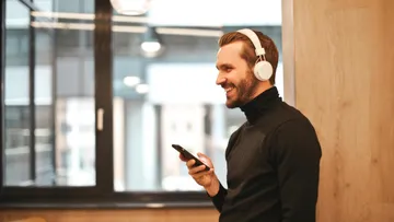 Man with headphones using smartphone, smiling indoors.