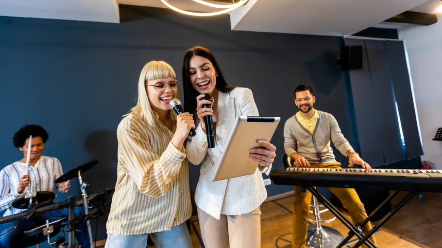 Zwei Frauen singen mit Mikrofonen; Musiker dahinter.