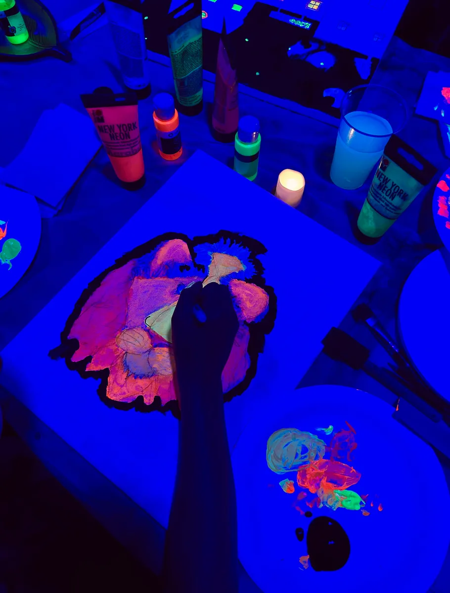 Person painting glowing artwork under blacklight.