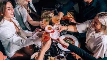 People toasting with cocktails at dinner table.