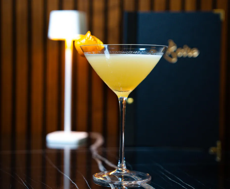 Cocktailglas mit orangem Getränk auf Tisch.